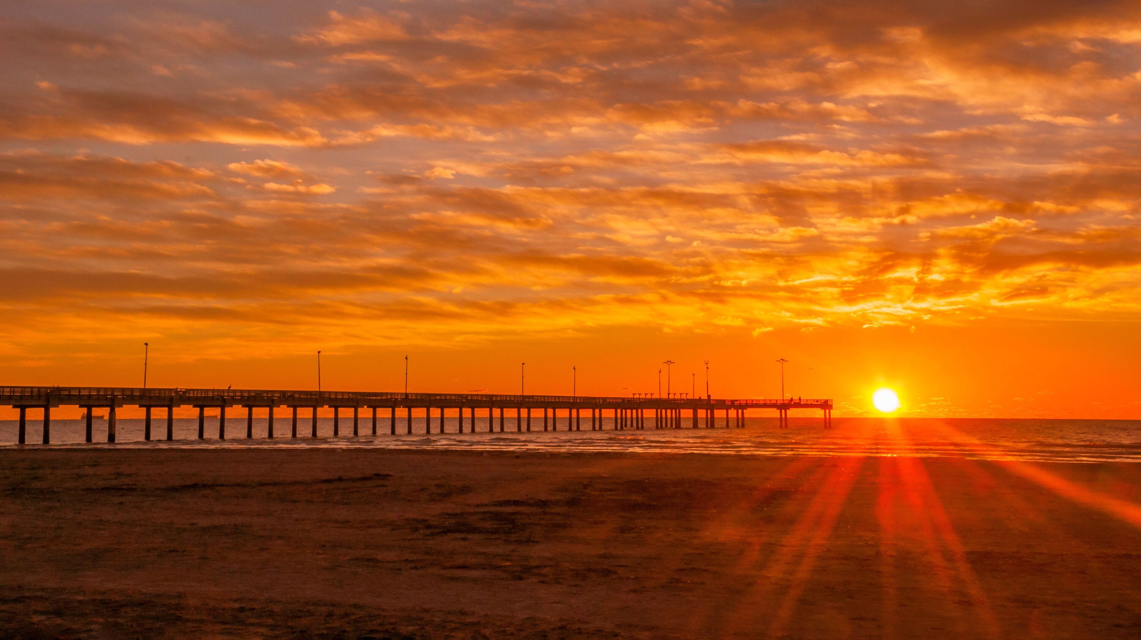 A sunset over a beach with a pier extending into the ocean.
