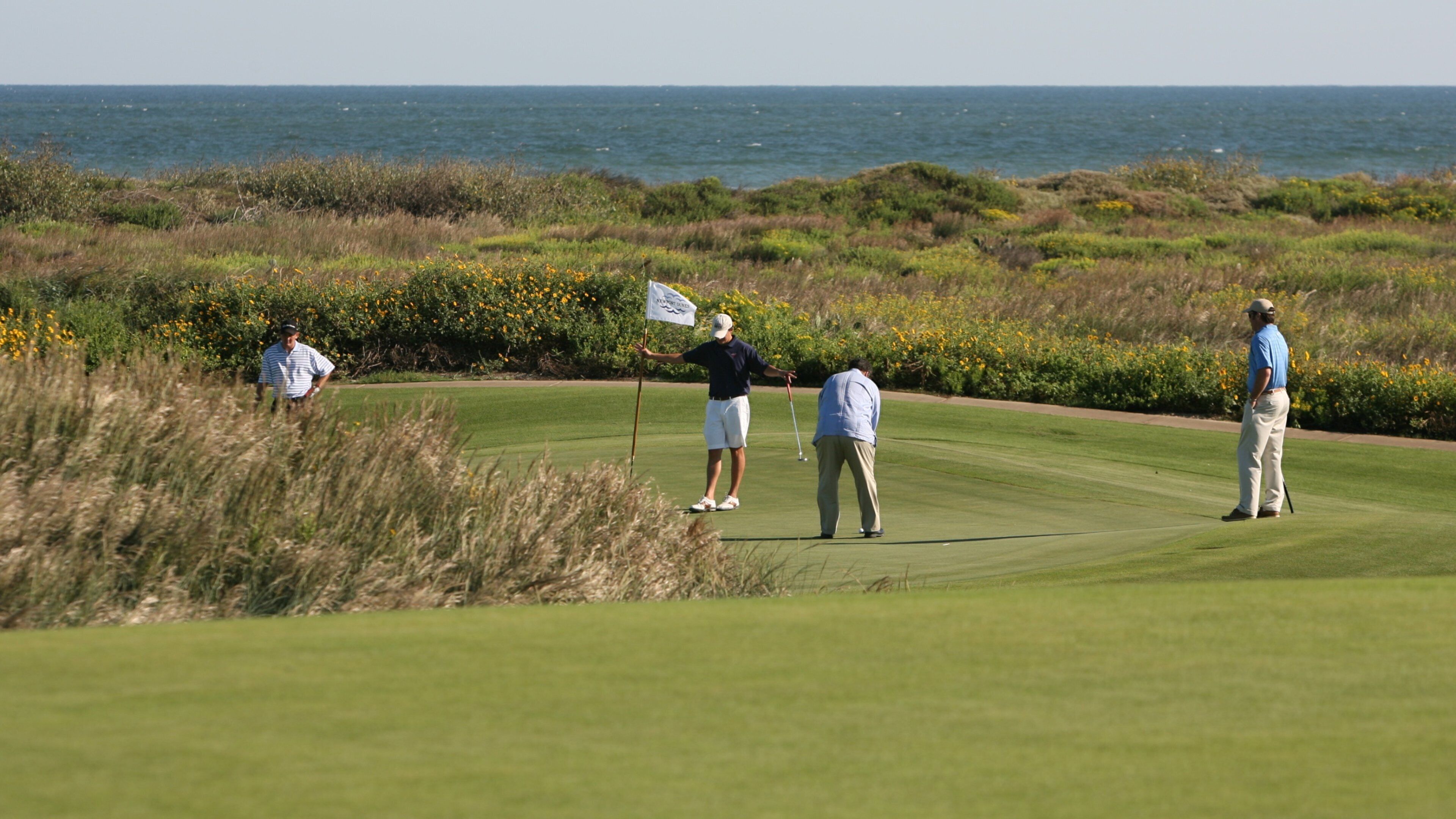 A golf course with players, ocean, and coastal vegetation.