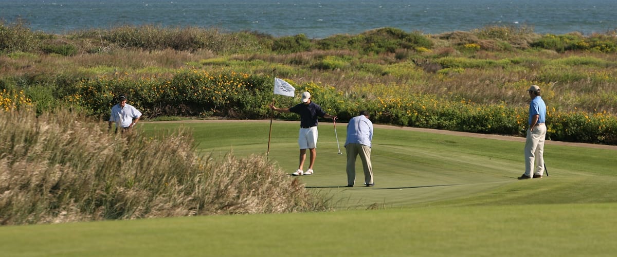 A golf course with players, ocean, and coastal vegetation.