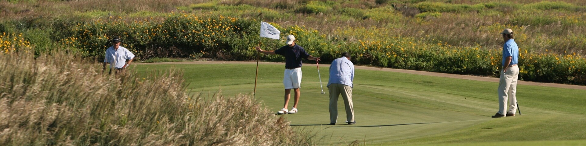 A golf course with players, ocean, and coastal vegetation.