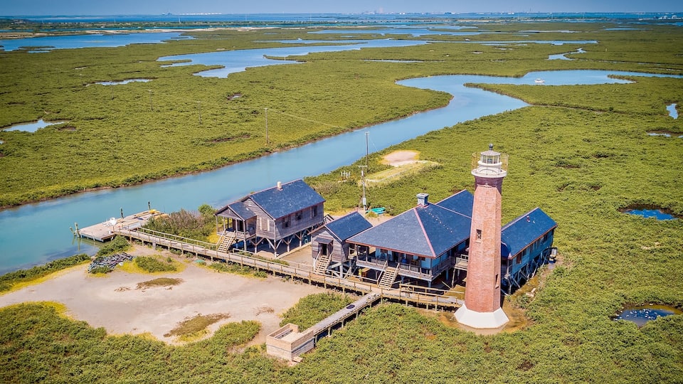 A coastal lighthouse with a pier, surrounded by marshland and a river.