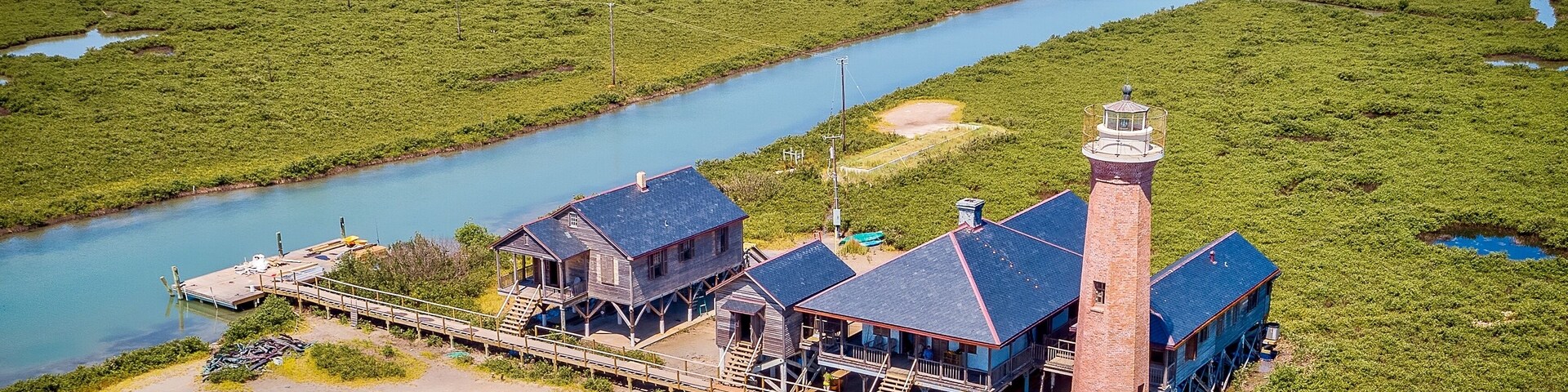 Un faro costero con un muelle, rodeado de humedales y un río.