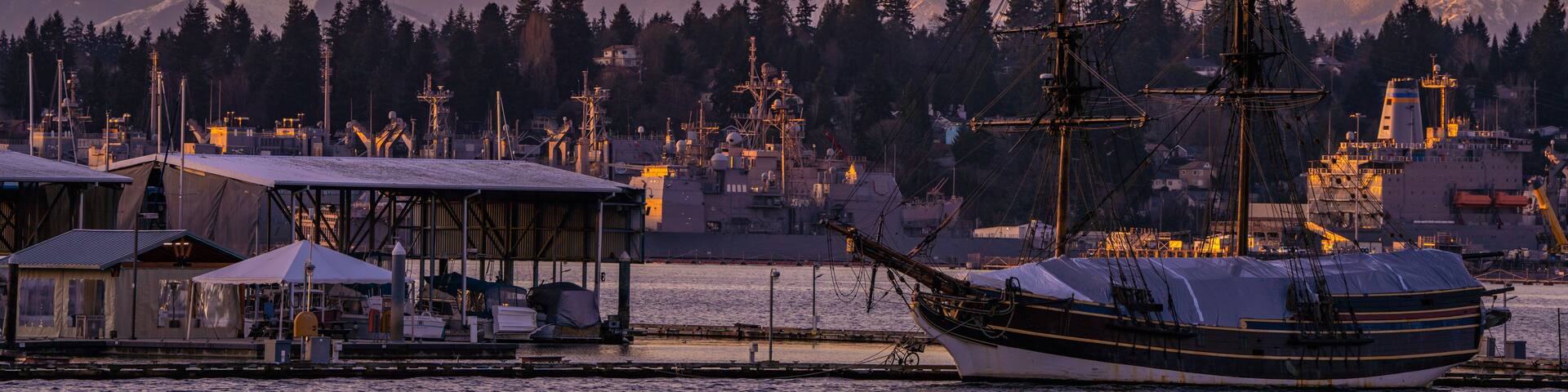 A sailing ship docked at a harbor with mountains in the background.