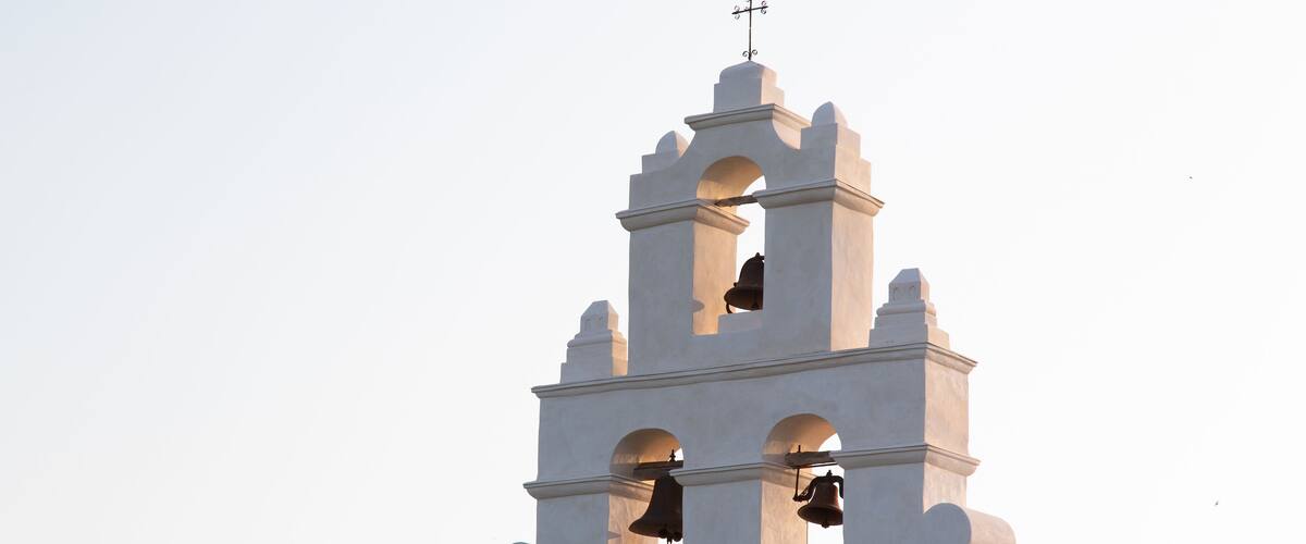 Un campanile bianco con una croce sulla sommità, diverse campane e finestre ad arco.