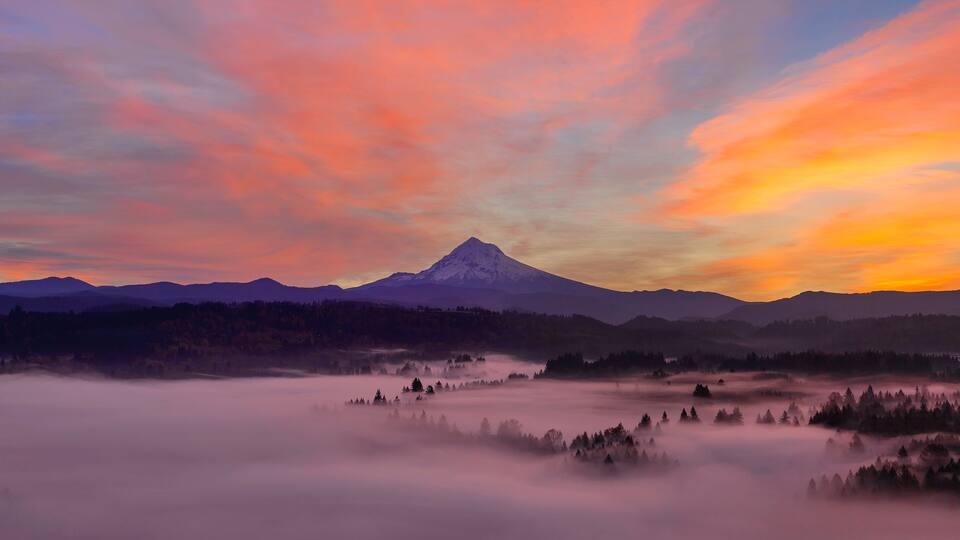 A mountain range with a prominent peak, surrounded by forested areas and a valley with mist.