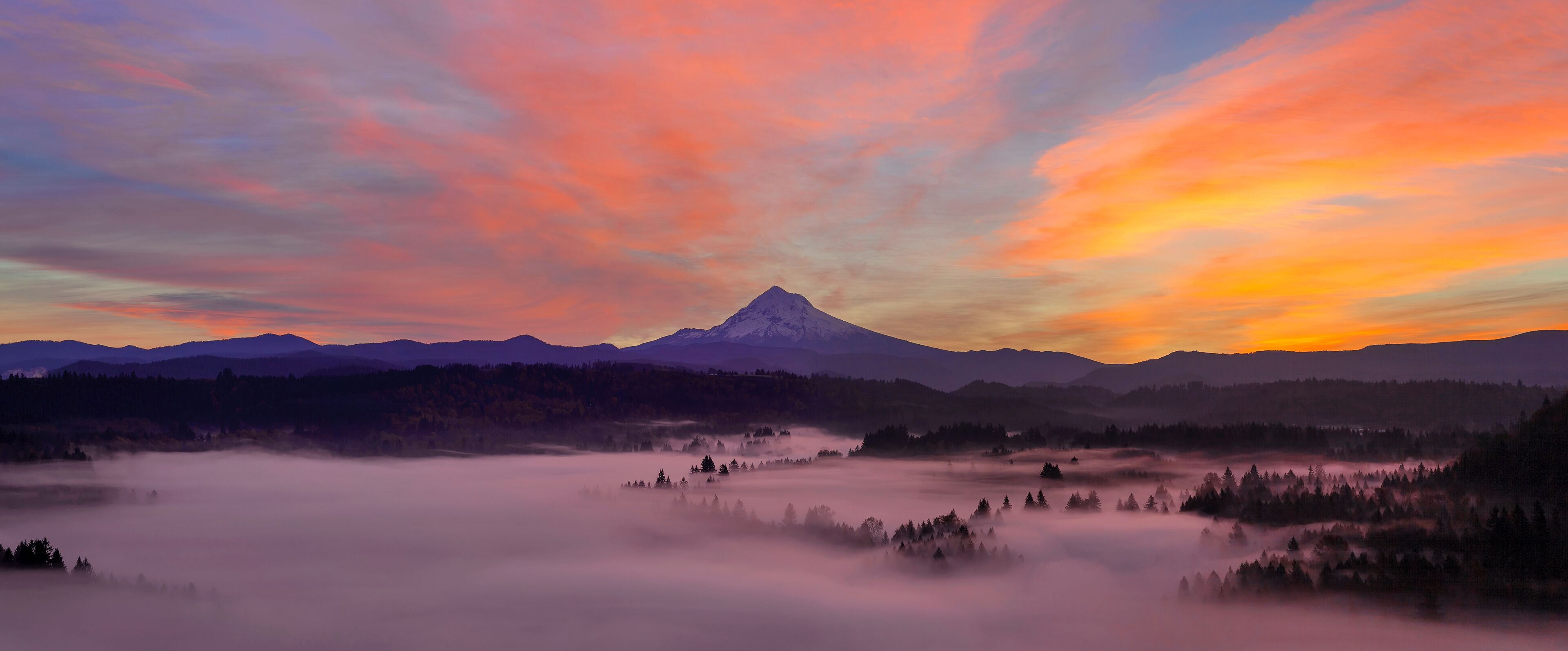 A mountain range with a prominent peak, surrounded by forested areas and a valley with mist.