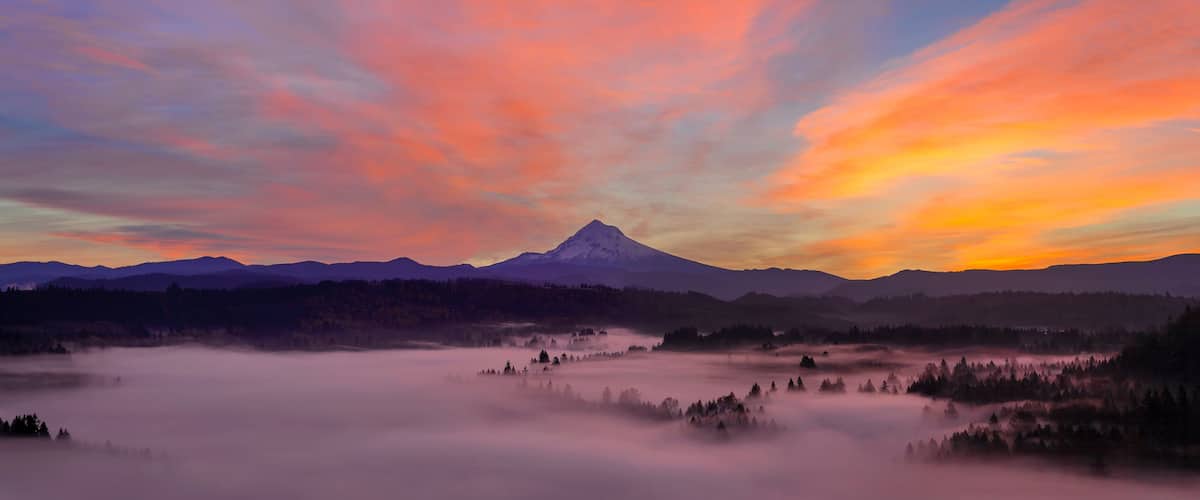 A mountain range with a prominent peak, surrounded by forested areas and a valley with mist.