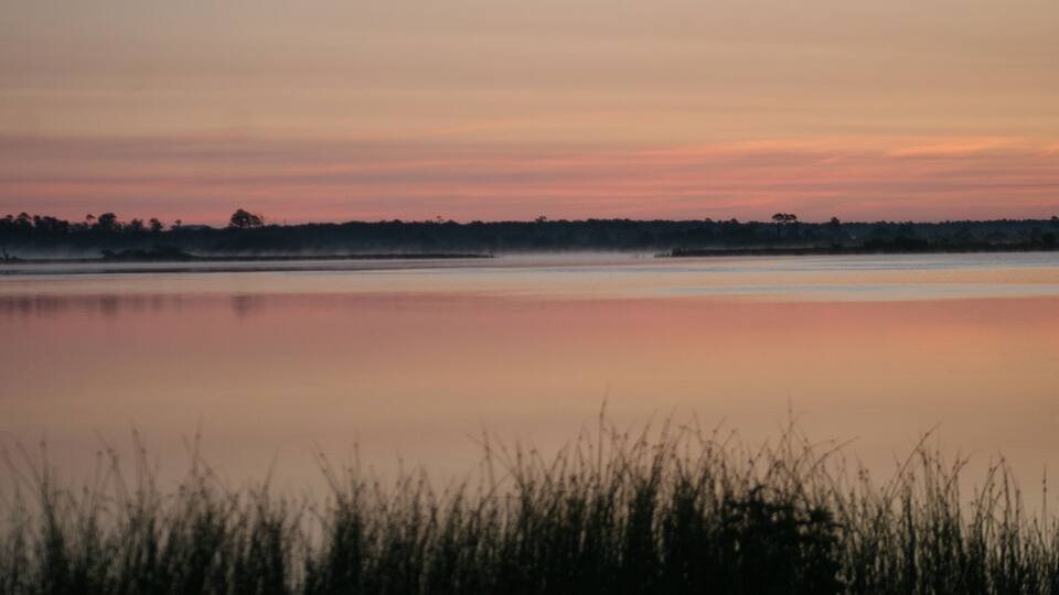 A calm lake at sunset with a silhouette of trees in the distance.