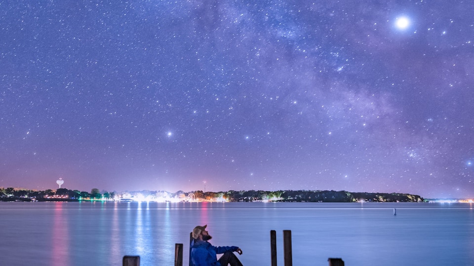 A wooden dock extending into a calm body of water under a starry night sky.