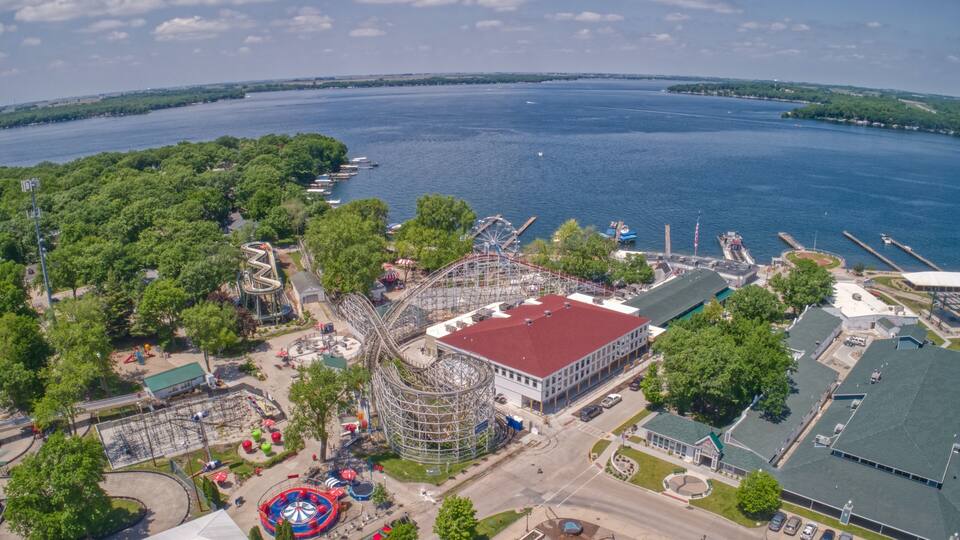 An aerial view of a park with a roller coaster, a Ferris wheel, and a body of water.