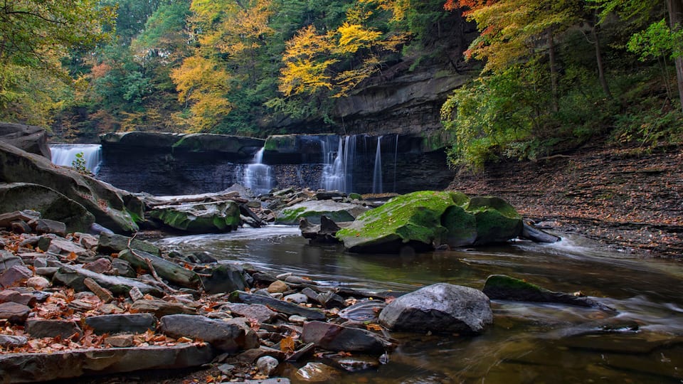 A waterfall cascading over rocks in a forested area with autumn-colored foliage.
