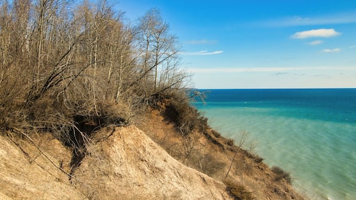 Under a sunny blue sky in early Spring, the view of a peaceful Lake Michigan as seen from atop a sandy, forested bluff at Lion's Den Gorge, near Grafton, WI.
