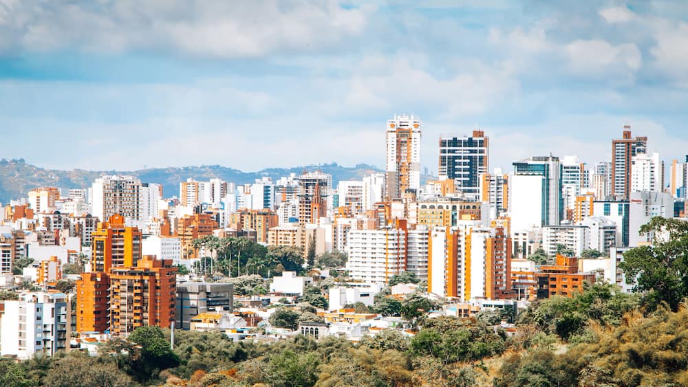 A cityscape with numerous high-rise buildings, a mix of modern and older architecture, and a backdrop of hills.