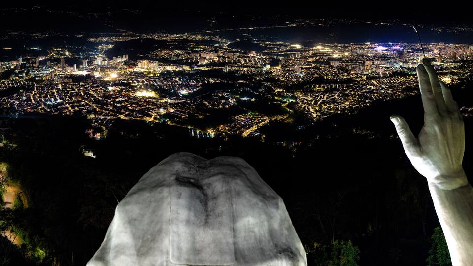 A nighttime cityscape with a large statue of a hand reaching towards the city lights.
