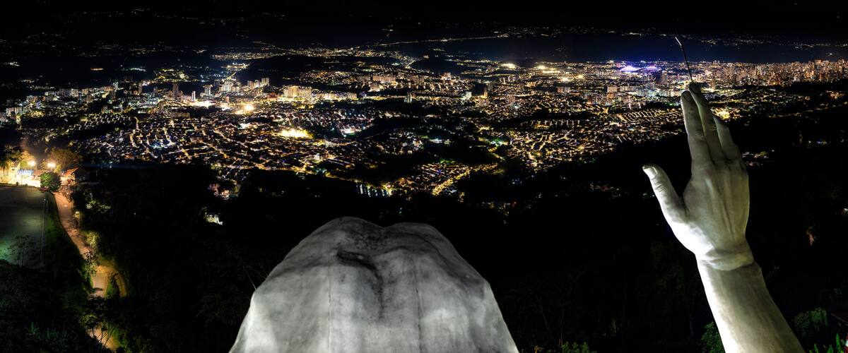 A nighttime cityscape with a large statue of a hand reaching towards the city lights.