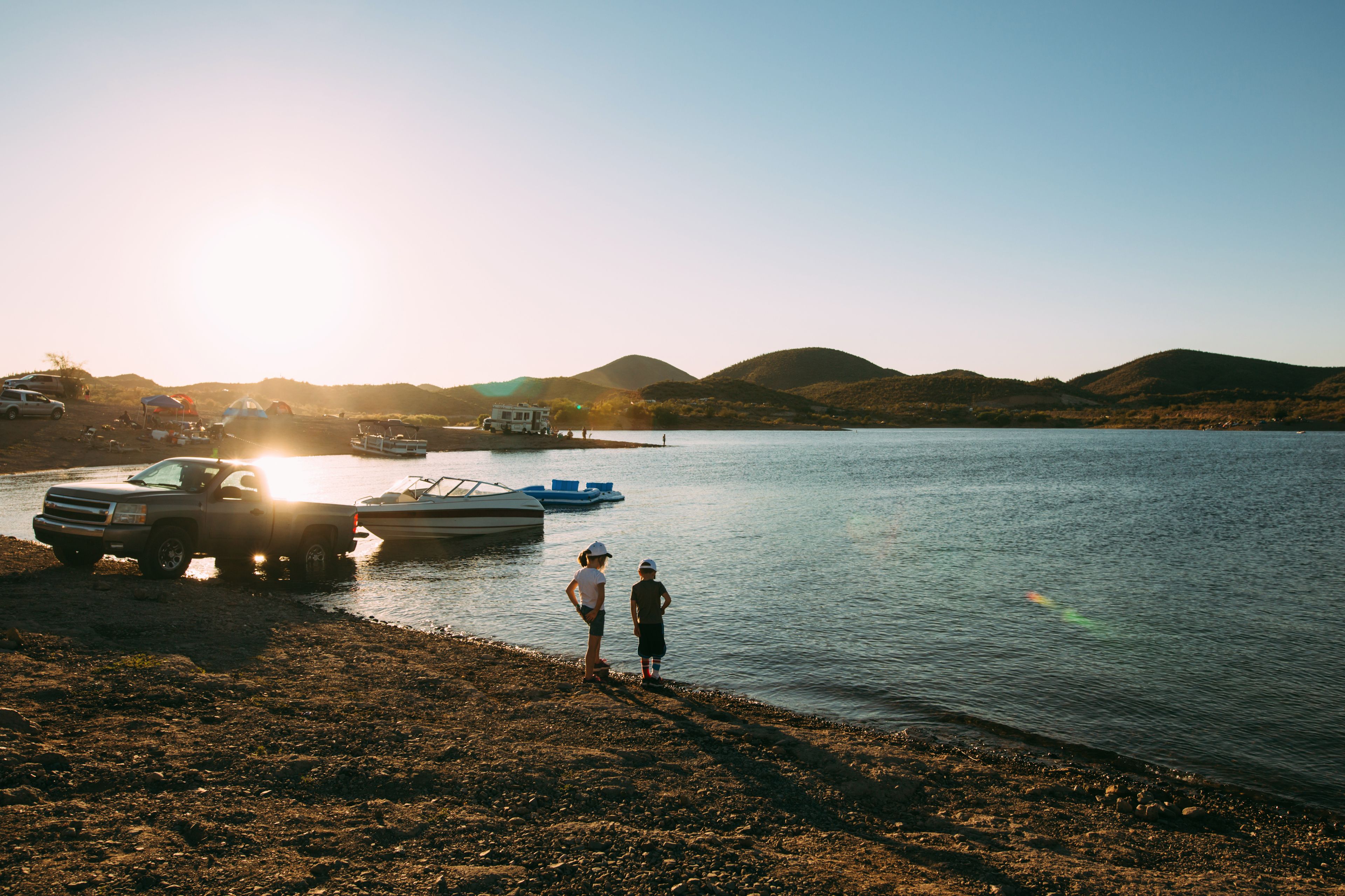 A lake with boats, a truck, and people on the shore during sunset.