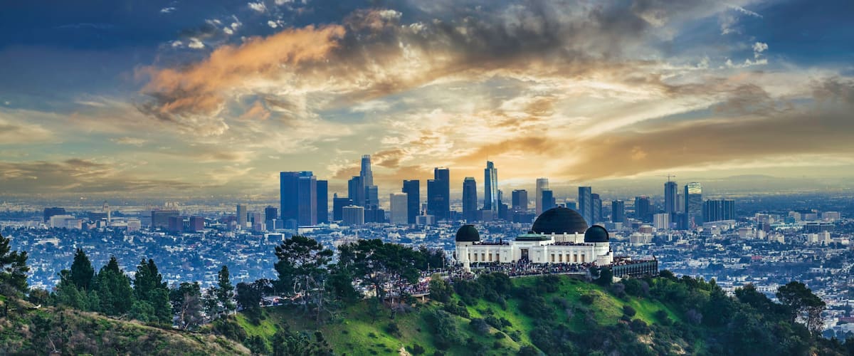 A city skyline with modern skyscrapers, a large dome structure, and a hill with greenery in the foreground.