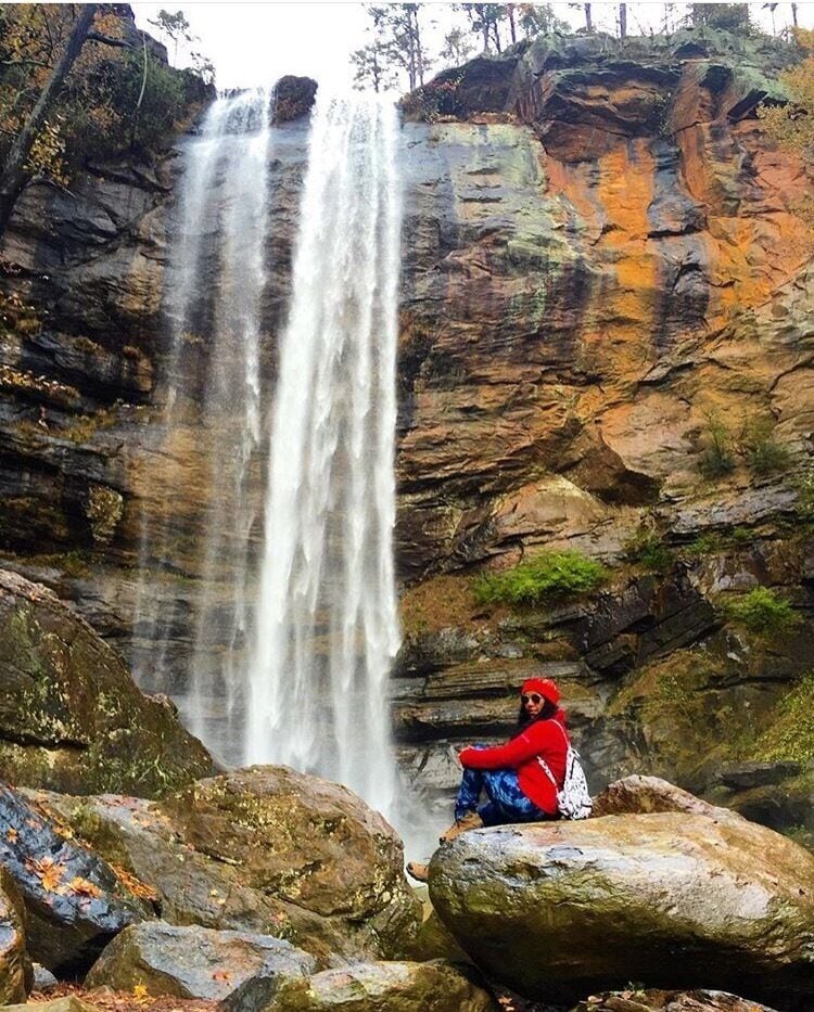 A waterfall cascading down a rocky cliff with a person sitting on a rock in the foreground.