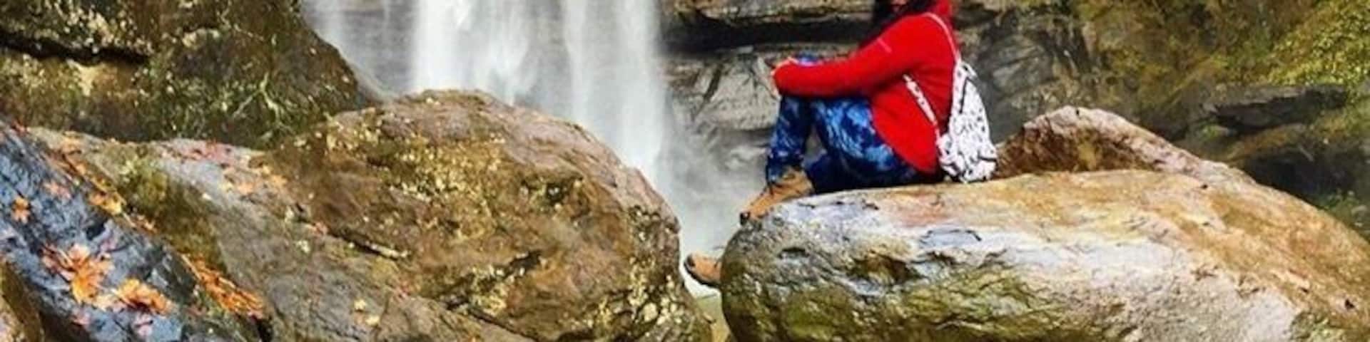 A waterfall cascading down a rocky cliff with a person sitting on a rock in the foreground.