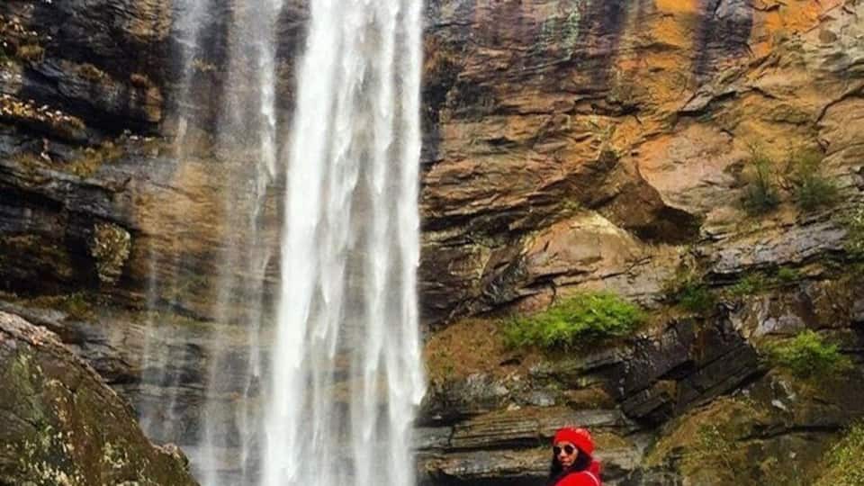 A waterfall cascading down a rocky cliff with a person sitting on a rock in the foreground.