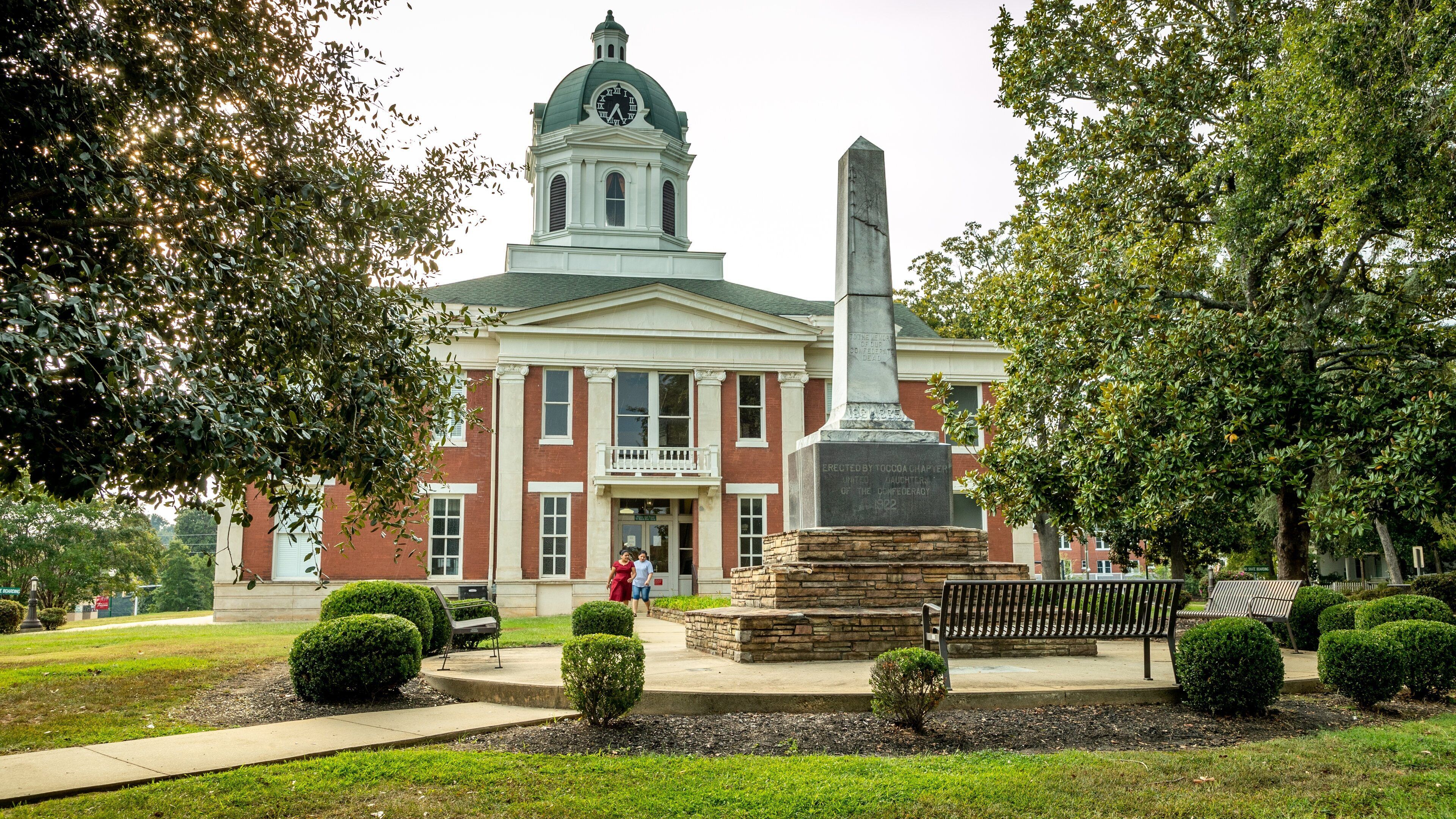 A historic building with a clock tower, a monument, and well-maintained landscaping.