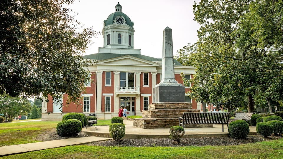 A historic building with a clock tower, a monument, and well-maintained landscaping.