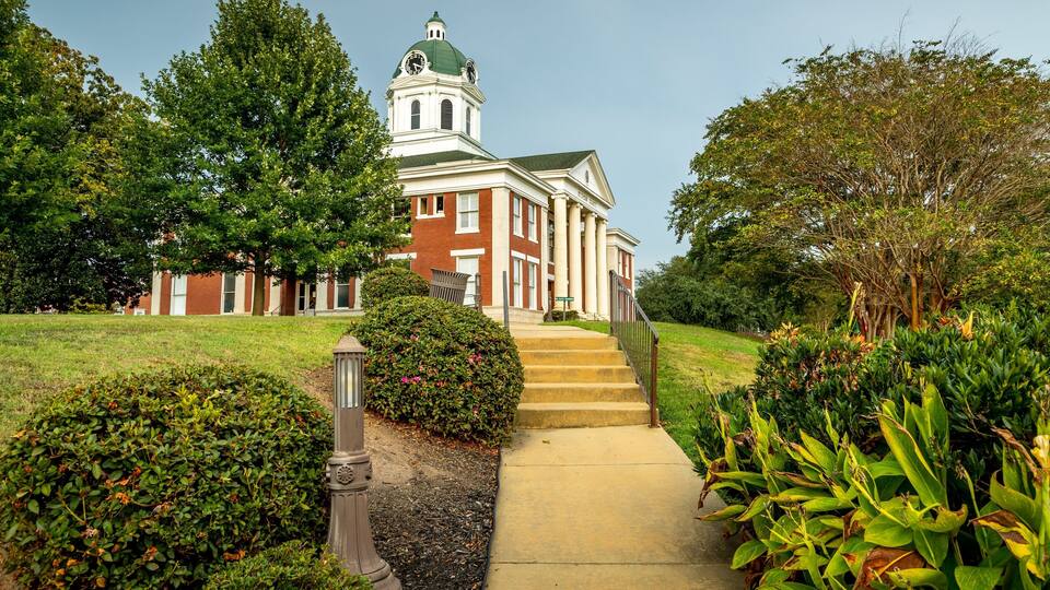 A historic building with a clock tower, surrounded by lush greenery and a well-maintained pathway.