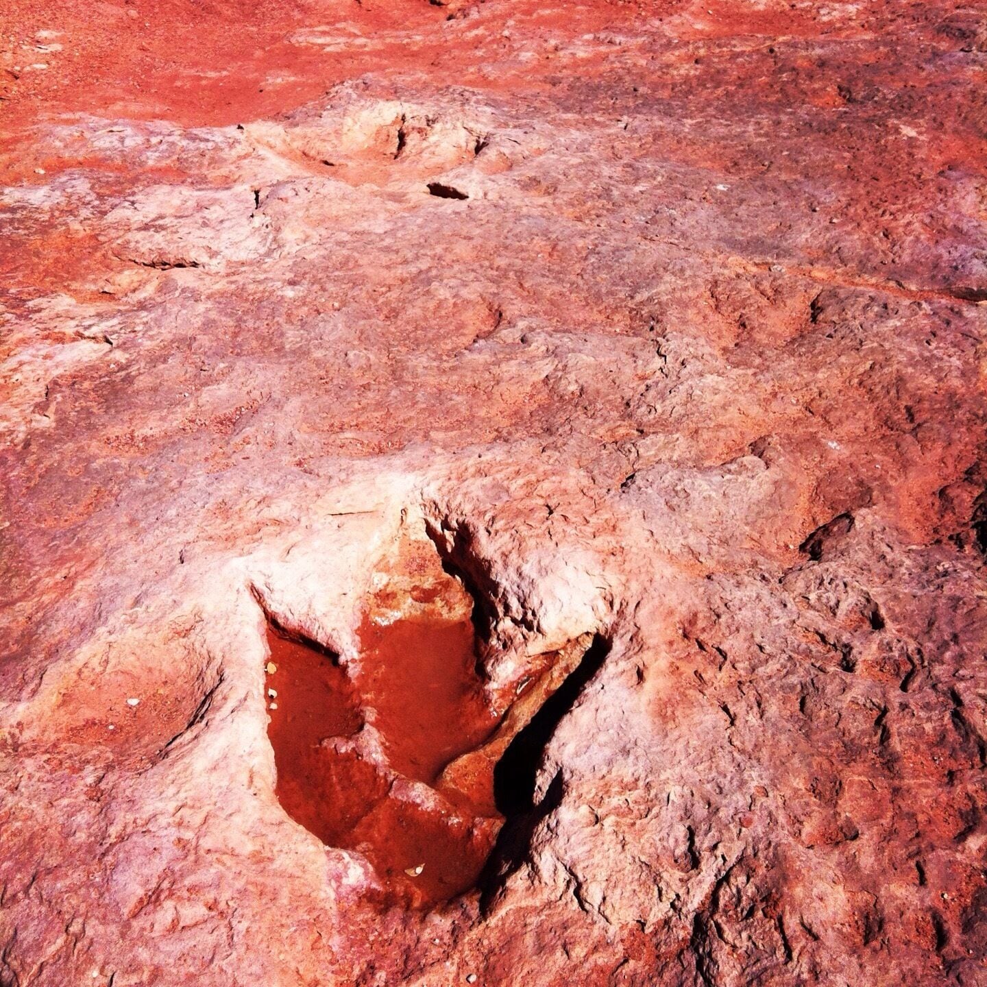 A rocky terrain with a prominent reddish-brown rock formation featuring a large, jagged opening.