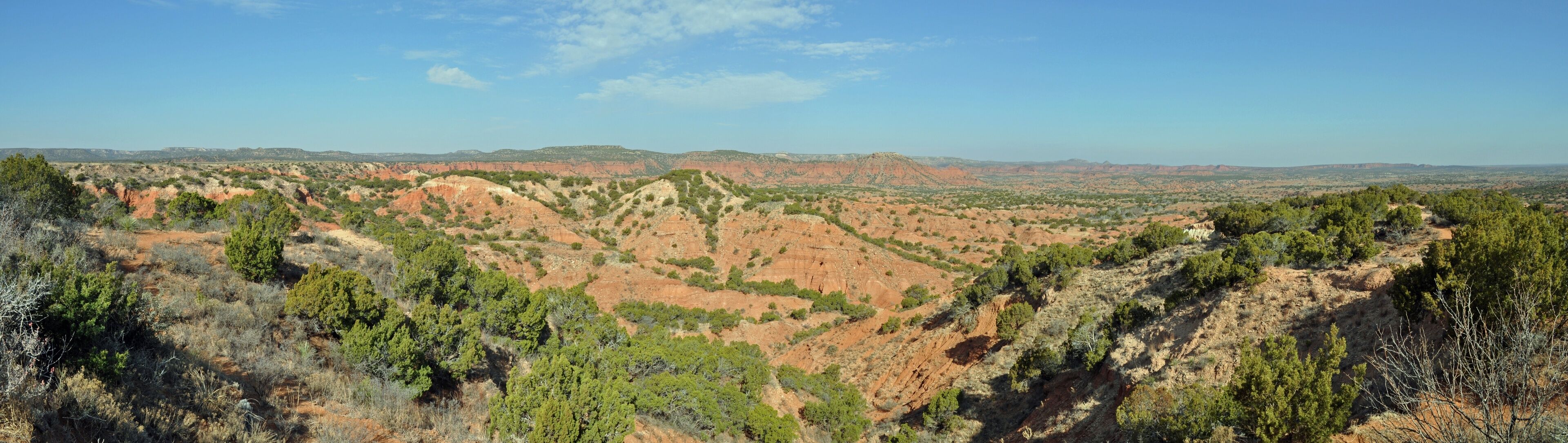 A rugged mountainous landscape with dense green vegetation and reddish-brown rock formations.
