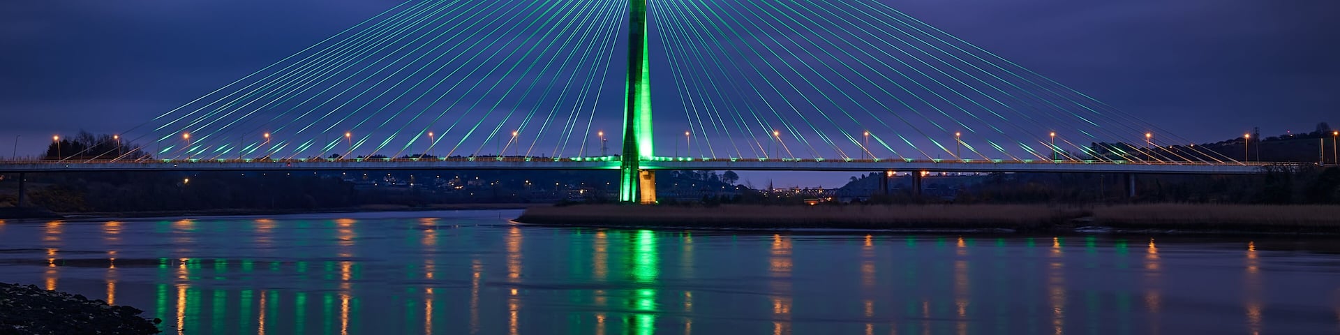 Modern line bridge illuminated with green lights for St. PAtricK in Waterford Ireland. Overnight.