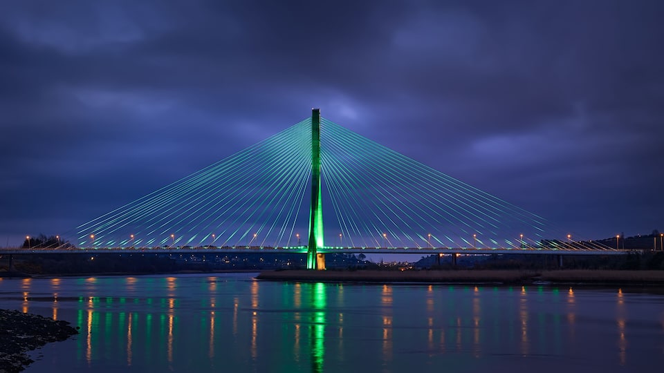 Modern line bridge illuminated with green lights for St. PAtricK in Waterford Ireland. Overnight.