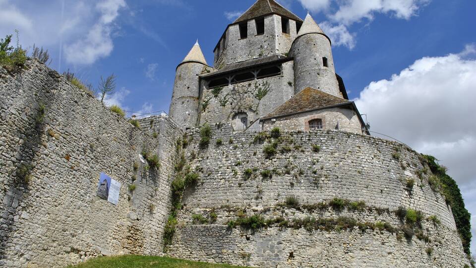 A medieval castle with stone walls, a tower, and a grassy hill.