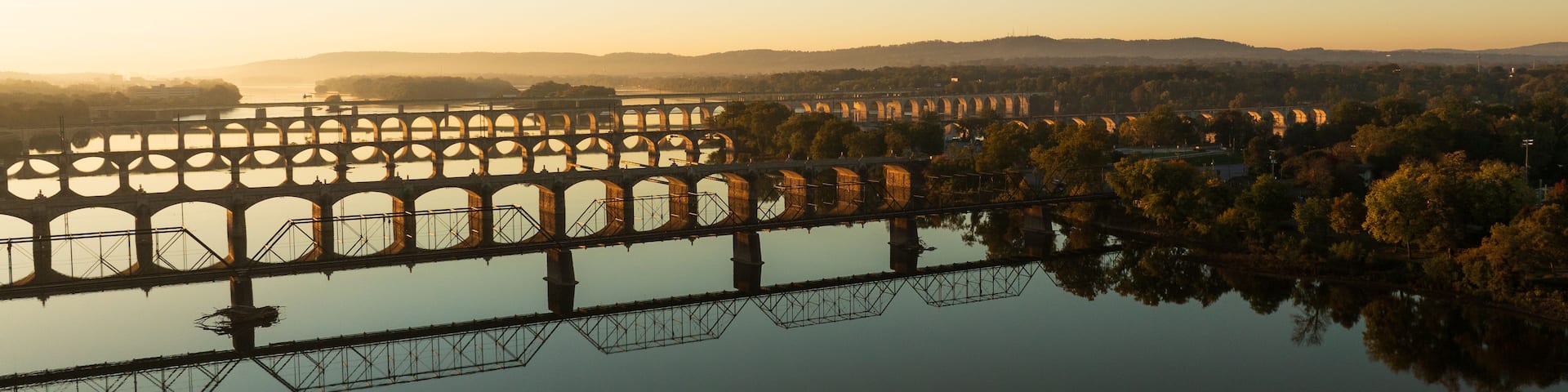 A bridge spanning a river with multiple arches, surrounded by trees and hills in the background.
