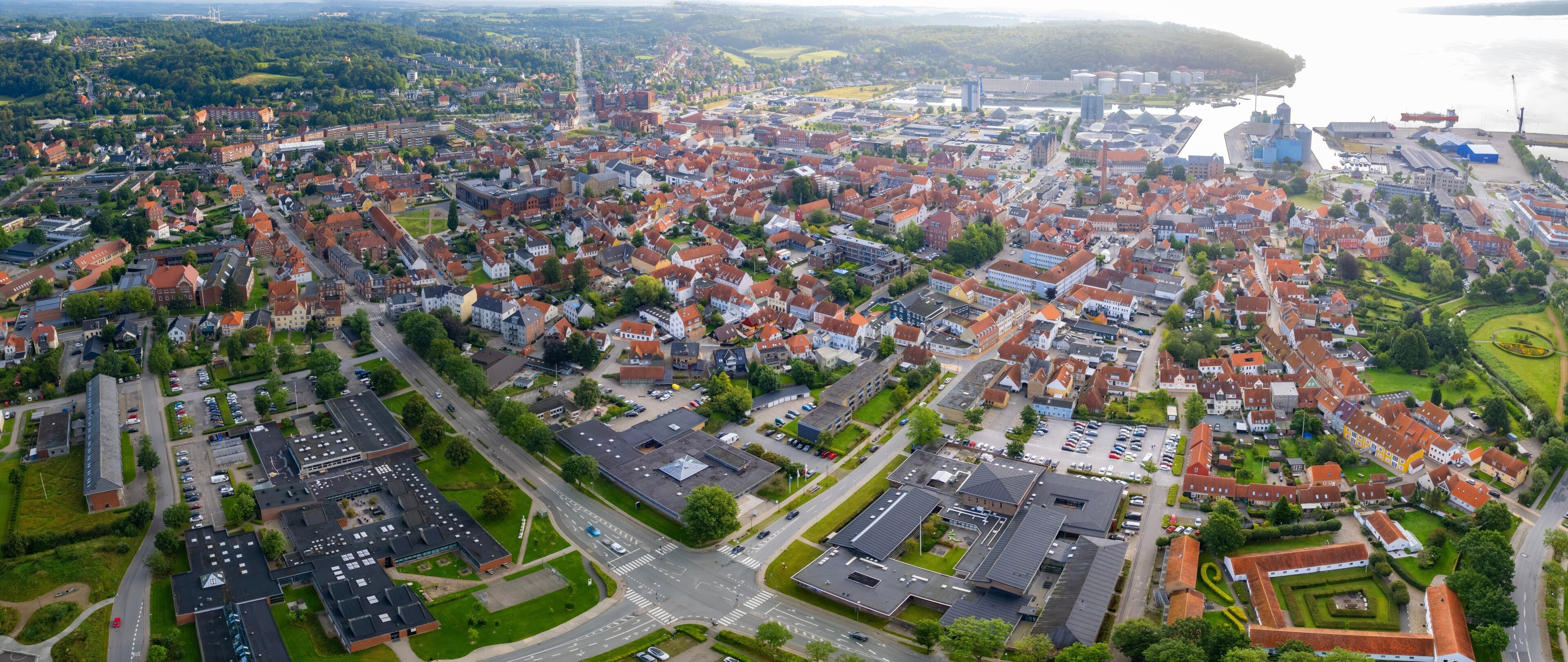 An aerial view of a densely populated town with red-roofed houses, a river, and industrial buildings.