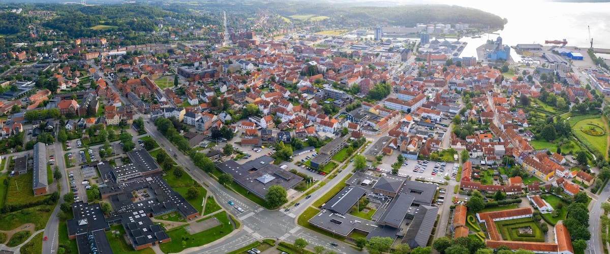 An aerial view of a densely populated town with red-roofed houses, a river, and industrial buildings.