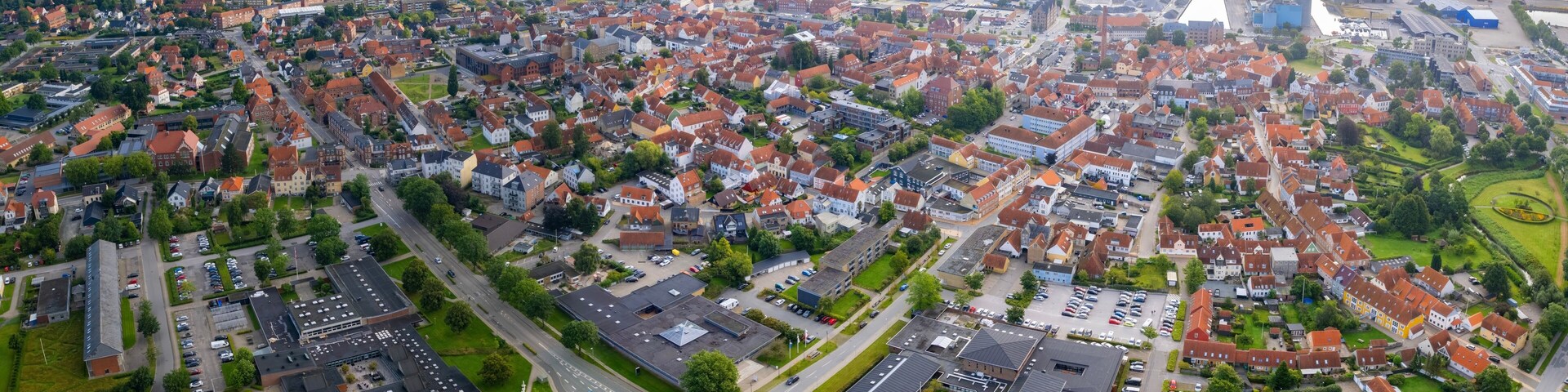 An aerial view of a densely populated town with red-roofed houses, a river, and industrial buildings.