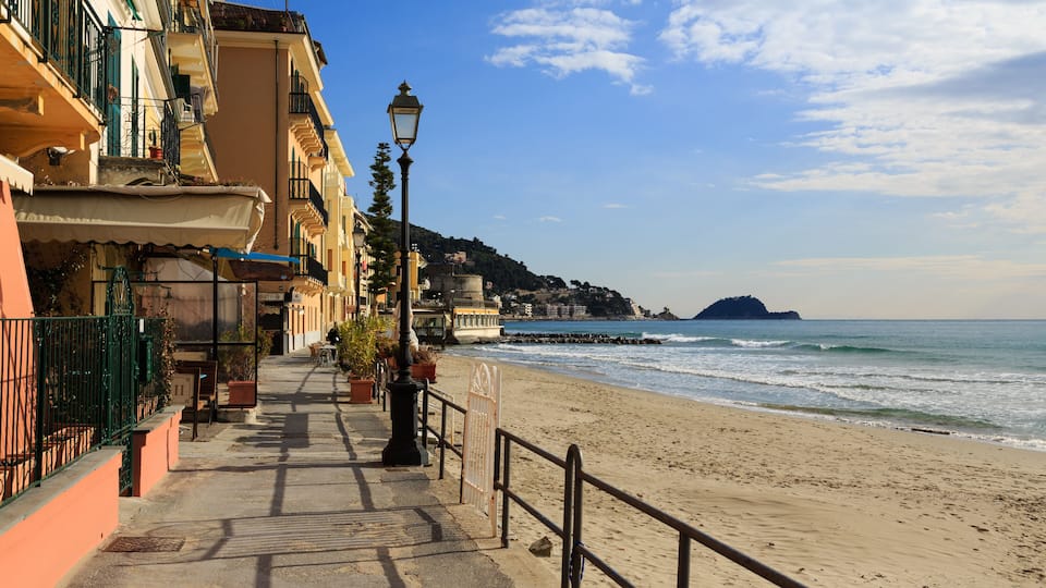 A seaside promenade with buildings, a lamp post, and a beach with waves.