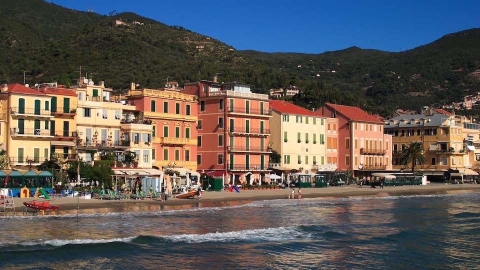 A coastal town with colorful buildings, a beach, and a mountain in the background.