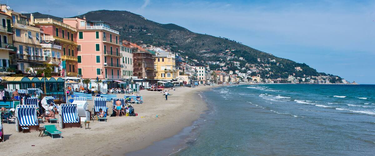 A coastal town with colorful buildings, a sandy beach, and a mountain in the background.