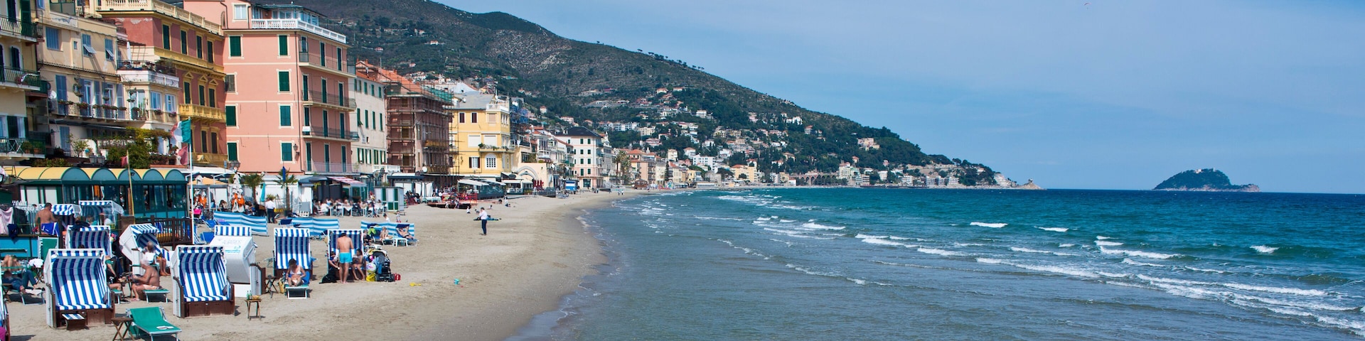 A coastal town with colorful buildings, a sandy beach, and a mountain in the background.