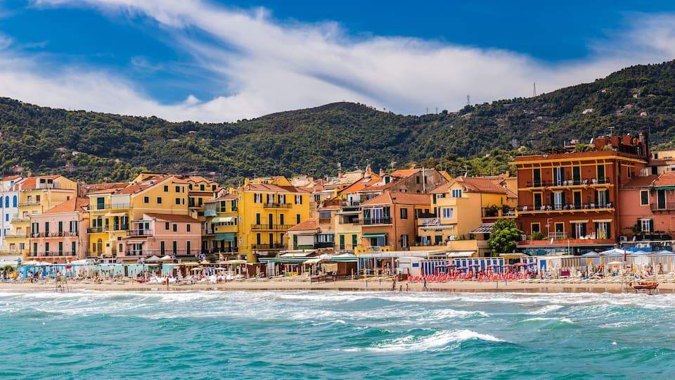 A coastal town with colorful buildings, a beach, and a mountainous backdrop.