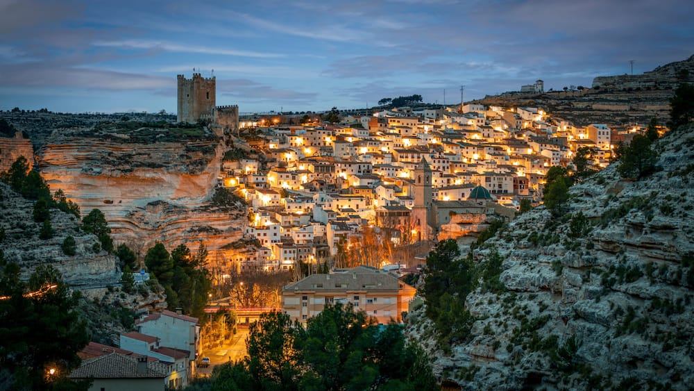 A town nestled in a valley with a prominent castle on a hill, surrounded by rocky terrain and dense vegetation.