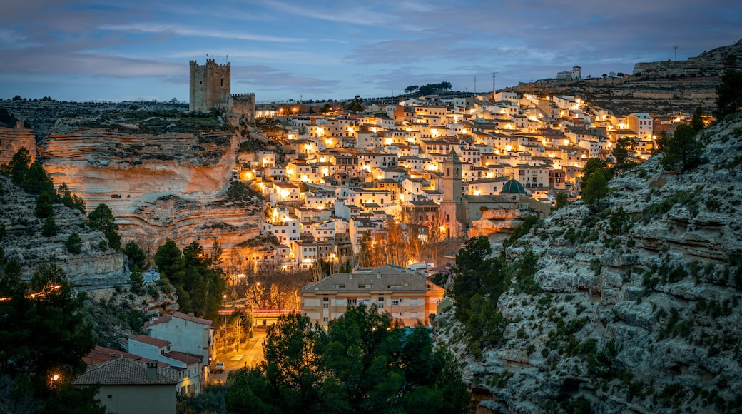 A town nestled in a valley with a prominent castle on a hill, surrounded by rocky terrain and dense vegetation.