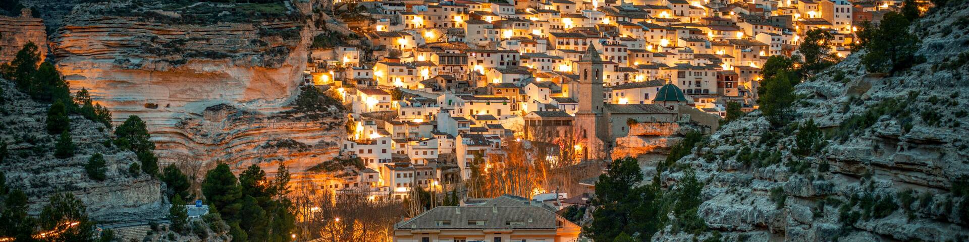 A town nestled in a valley with a prominent castle on a hill, surrounded by rocky terrain and dense vegetation.