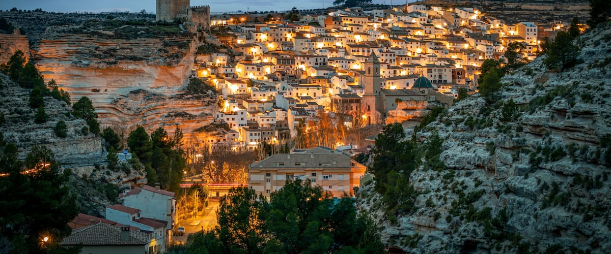A town nestled in a valley with a prominent castle on a hill, surrounded by rocky terrain and dense vegetation.