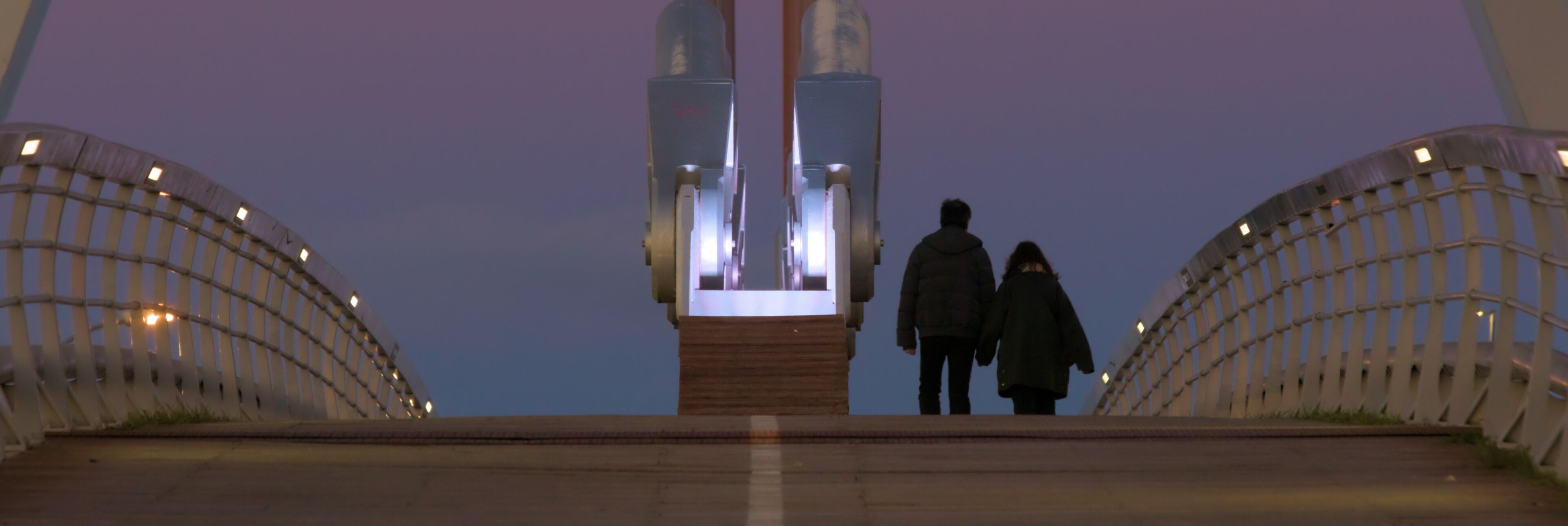 A bridge with a central monument and two people walking on it.