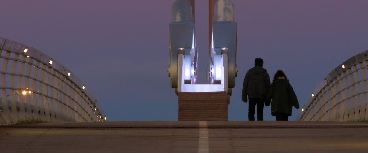 A bridge with a central monument and two people walking on it.