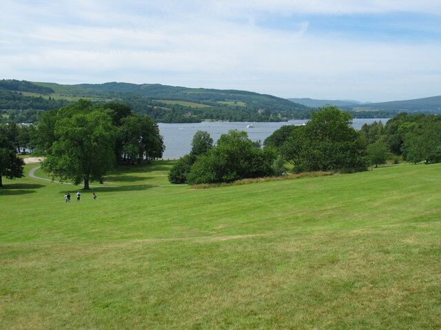 Un campo cubierto de hierba con un lago y colinas al fondo.