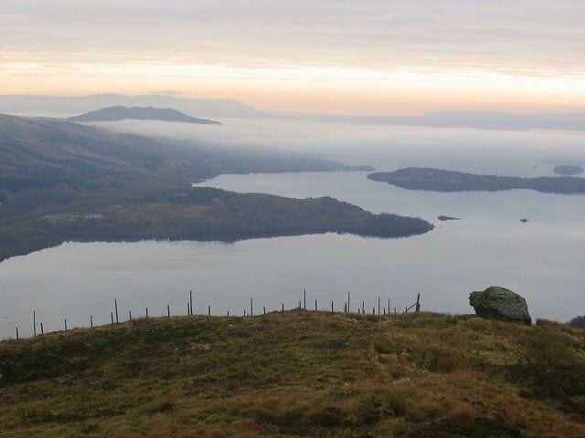 Boulder, Stob Gobhlach. Large boulder (the fence is a high deer fence) overlooking Loch Lomond. The southern end of the loch is under a fogbank.