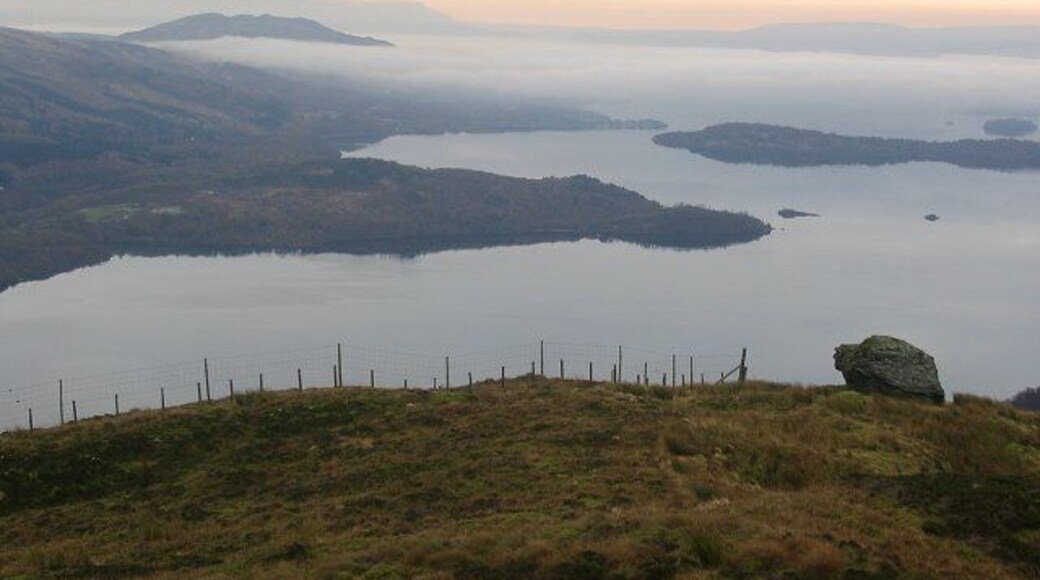 Boulder, Stob Gobhlach. Large boulder (the fence is a high deer fence) overlooking Loch Lomond. The southern end of the loch is under a fogbank.